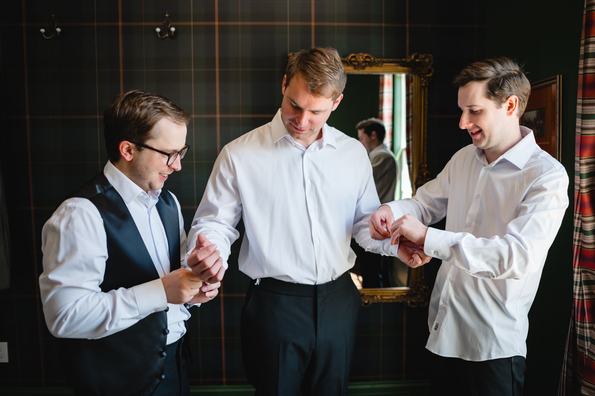 Groomsmen in white shirts helping each other with cufflinks before wedding ceremony.