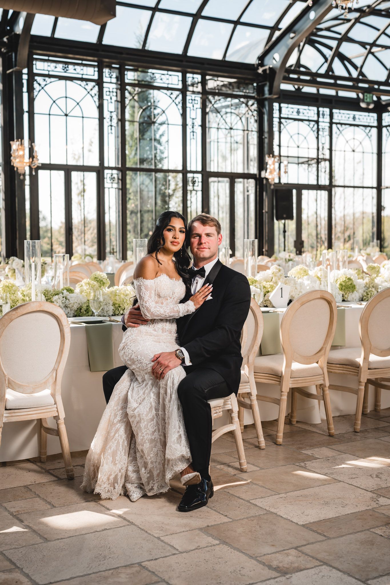 Bride and groom posing inside a stunning glass greenhouse wedding reception hall.