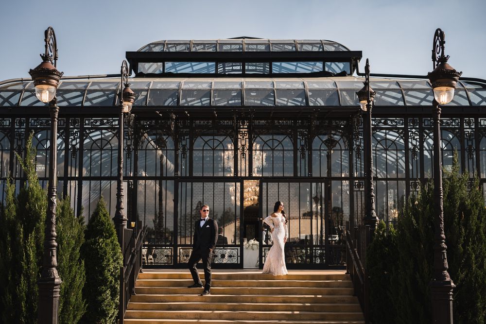 Elegant wedding couple descends grand steps before stunning Victorian glass greenhouse venue.