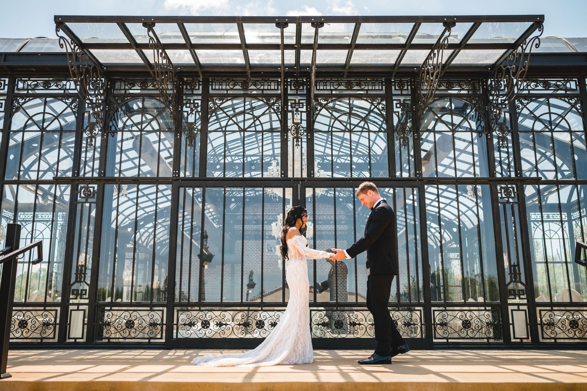 Bride and groom dancing in front of an elegant black iron greenhouse wedding venue.