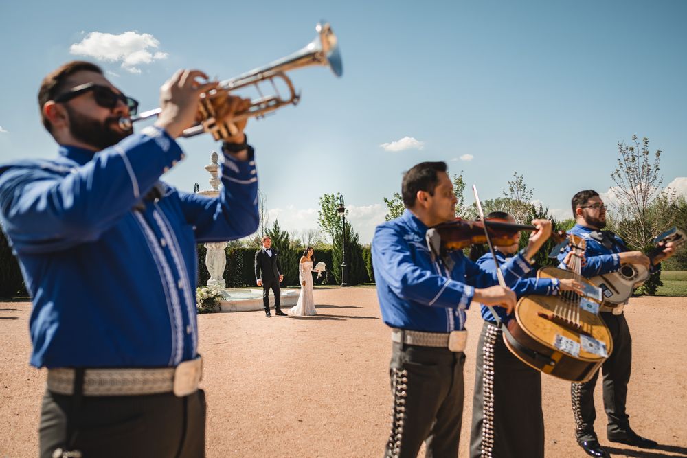 Mariachi band in blue suits playing trumpet and violin at an outdoor wedding ceremony.