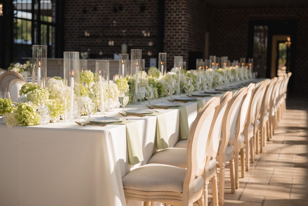 Long reception table with white linens, green hydrangeas, and tall glass candle holders.