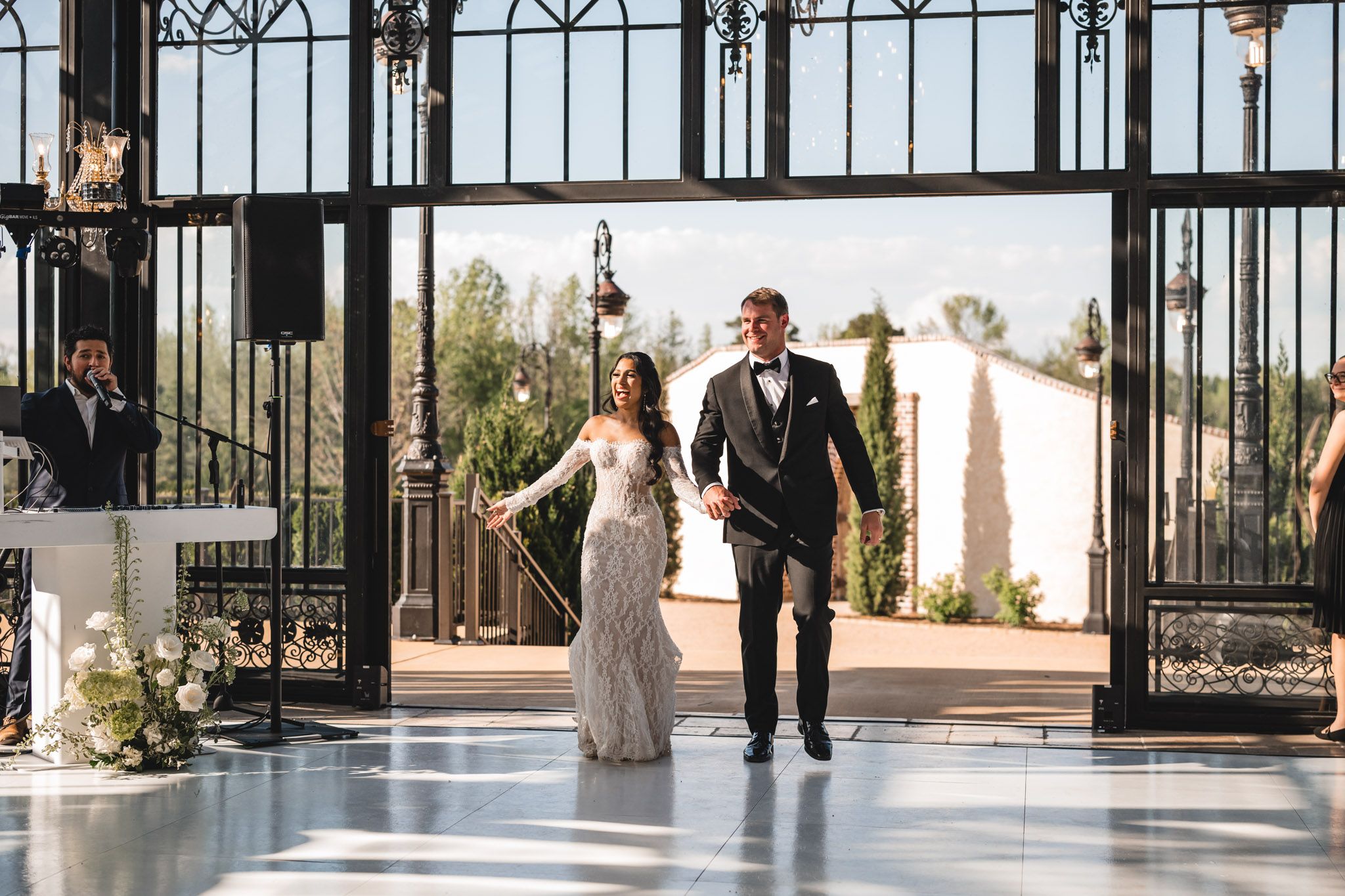 Bride and groom enter elegant glass and iron reception hall holding hands after ceremony.