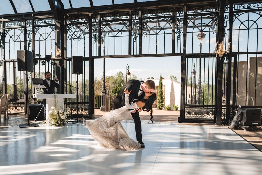 Bride and groom share elegant first dance dip in a stunning glass greenhouse wedding venue.