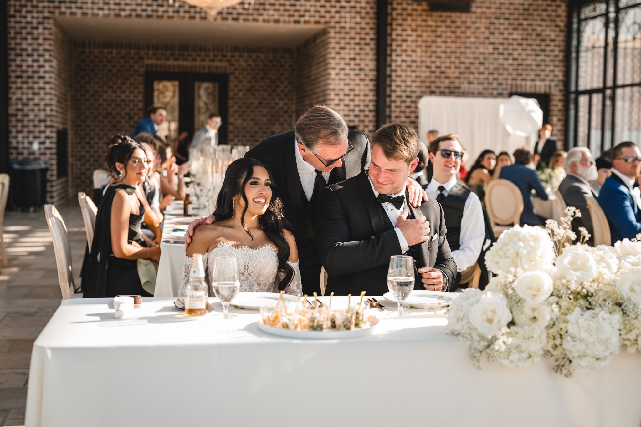 Bride and groom share an intimate moment at wedding reception head table with white floral arrangements.