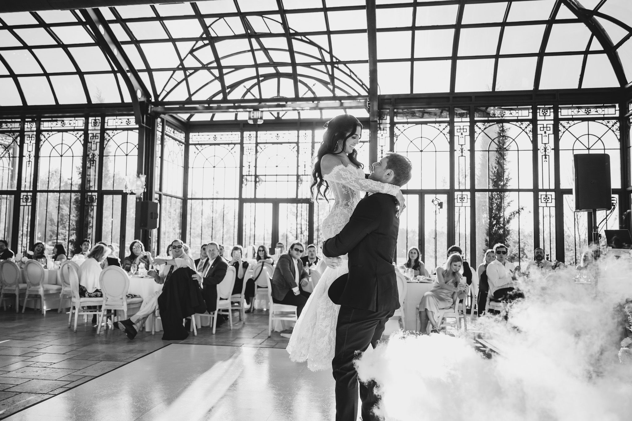 Groom lifts bride during first dance in a stunning glass conservatory reception venue.