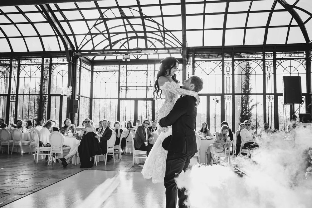 Groom lifts bride during first dance in a stunning glass conservatory reception venue.