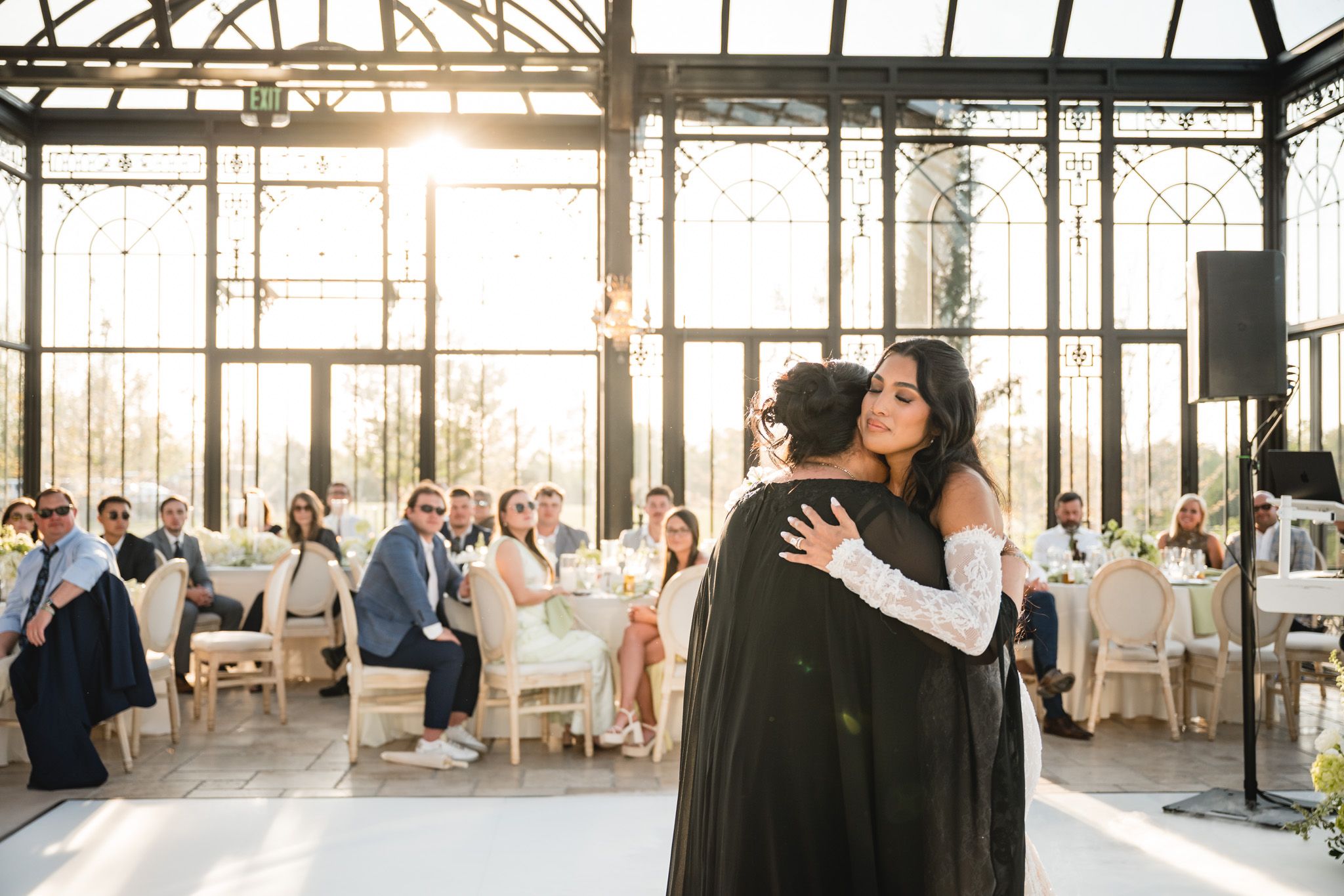 Bride shares an emotional dance with a guest in a sunlit greenhouse wedding reception.