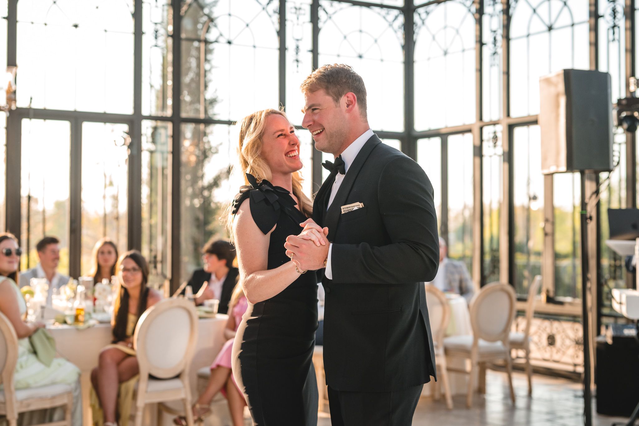 Couple laughs and dances together at a wedding reception in a glass conservatory venue.
