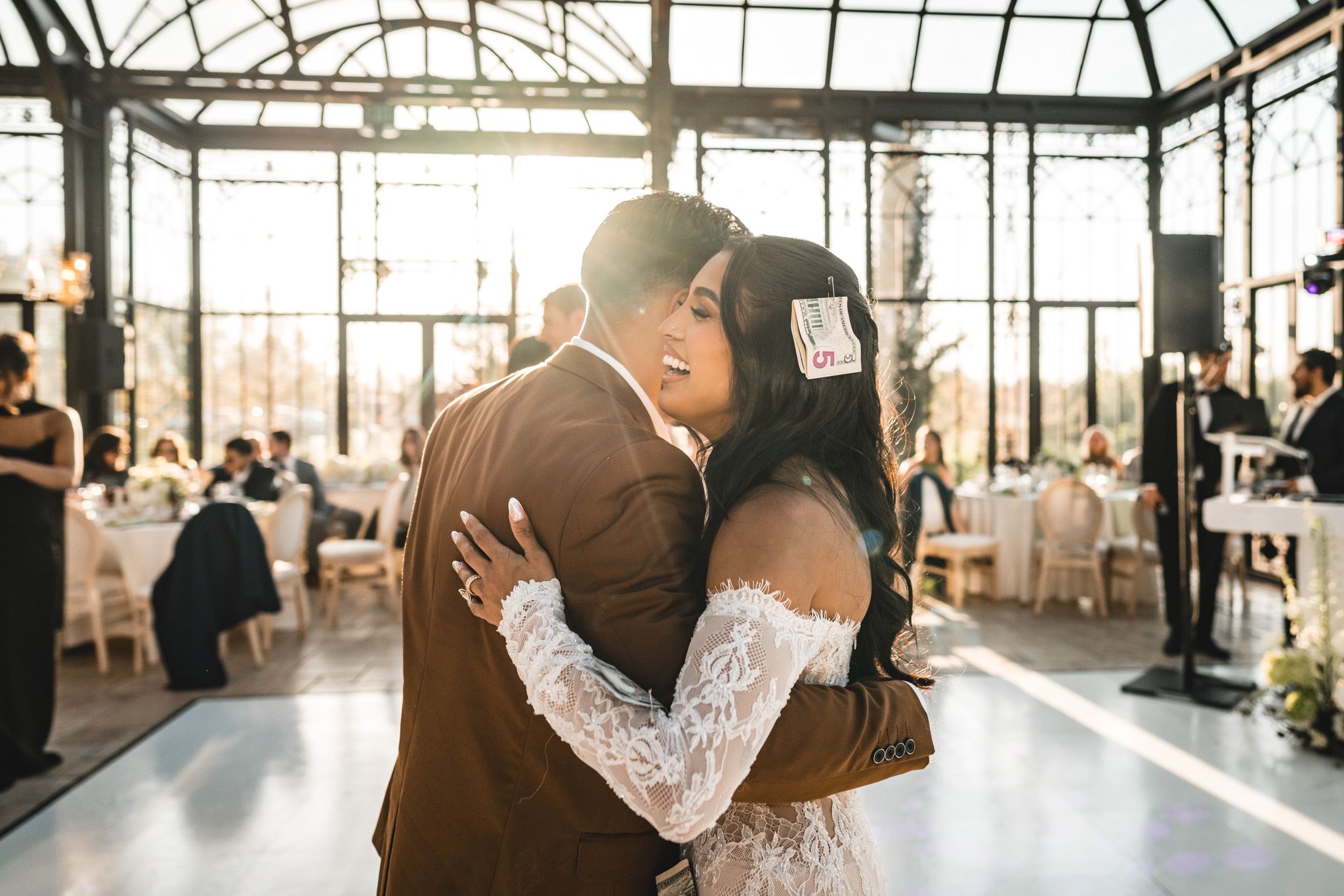 Bride and groom share an emotional first dance embrace in a stunning sunlit greenhouse wedding venue.