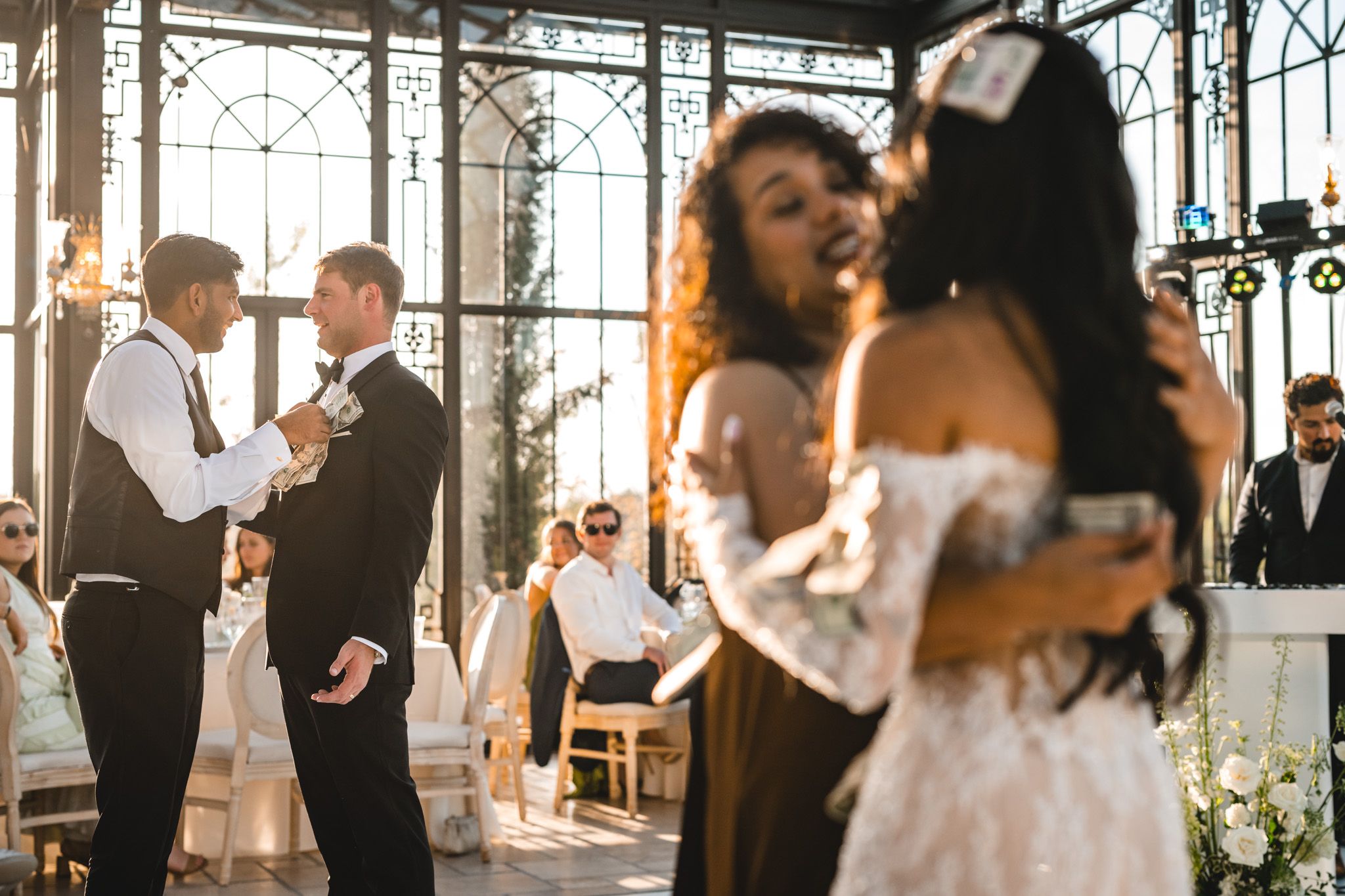 Wedding guests embrace and celebrate during reception in a beautiful glass greenhouse venue.