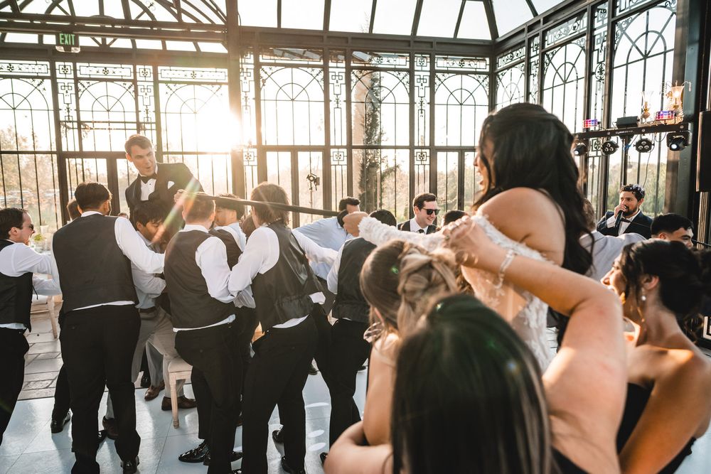 Wedding guests dance together in a stunning sunlit glass greenhouse reception hall.