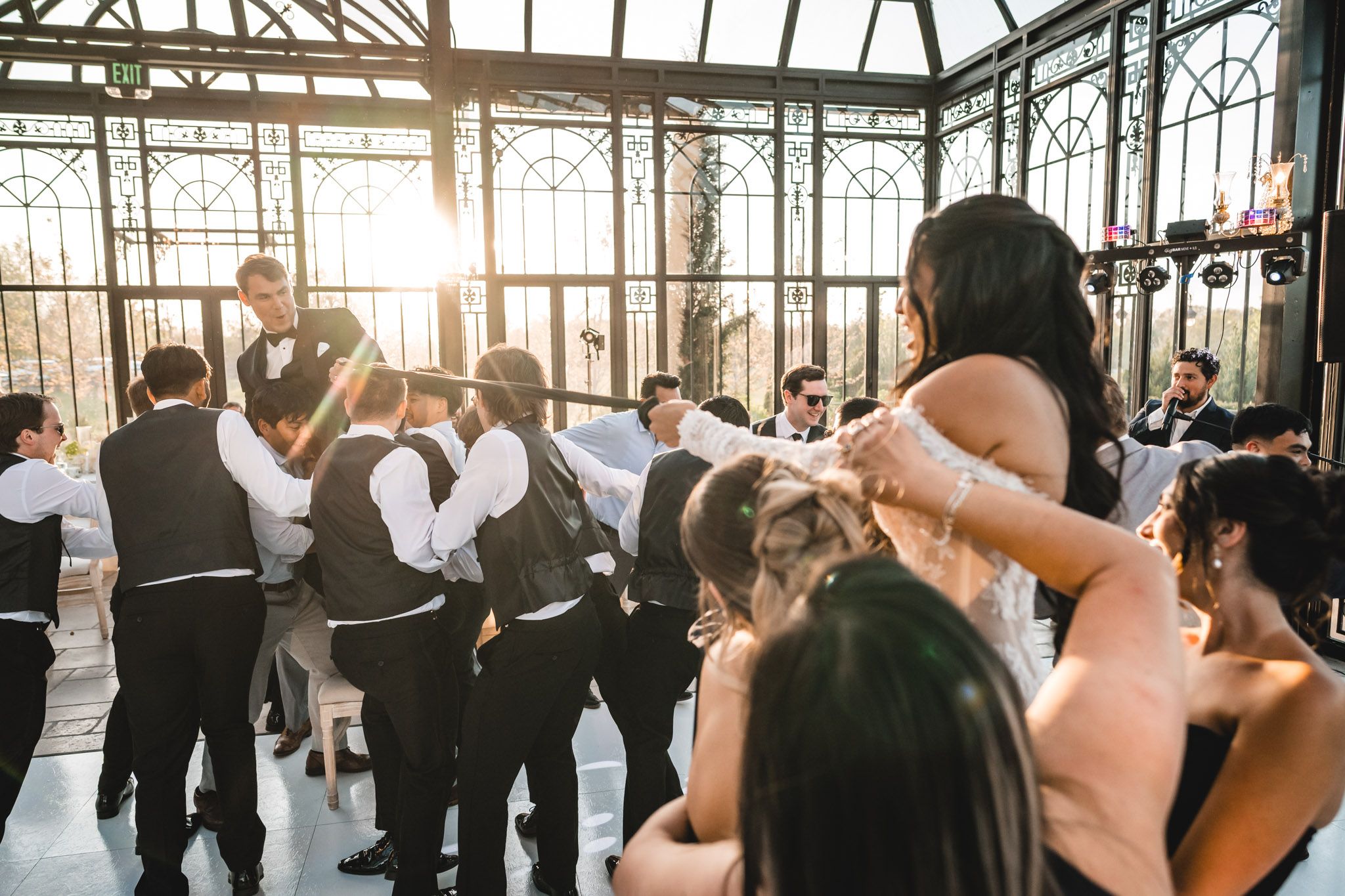 Wedding guests dance together in a stunning sunlit glass greenhouse reception hall.