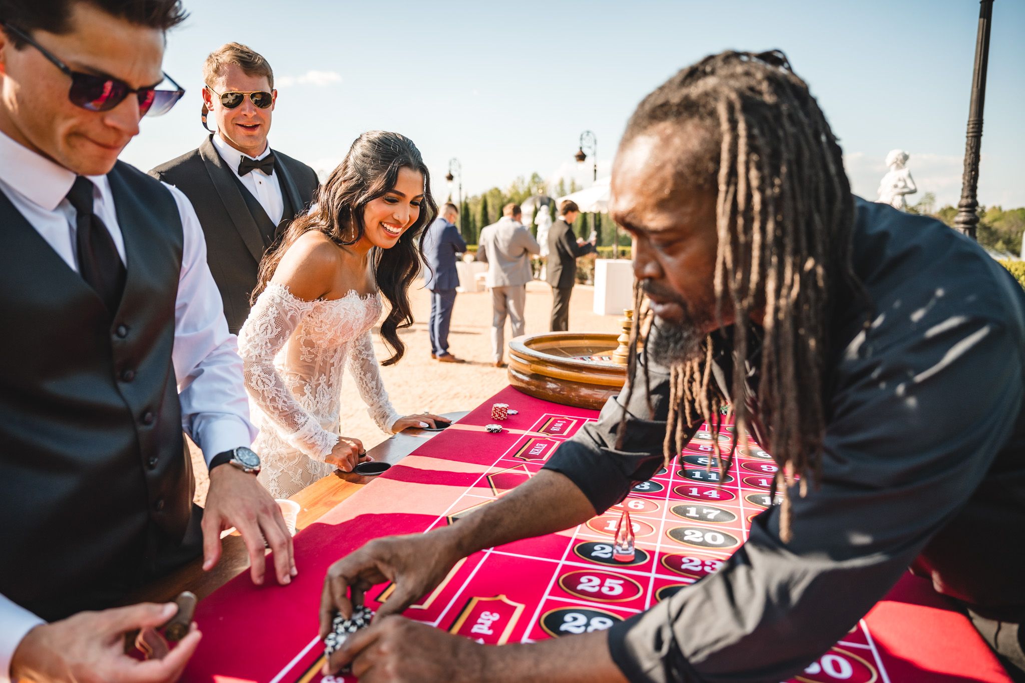 Guests play roulette at a casino-themed wedding reception with a bride in a lace gown.