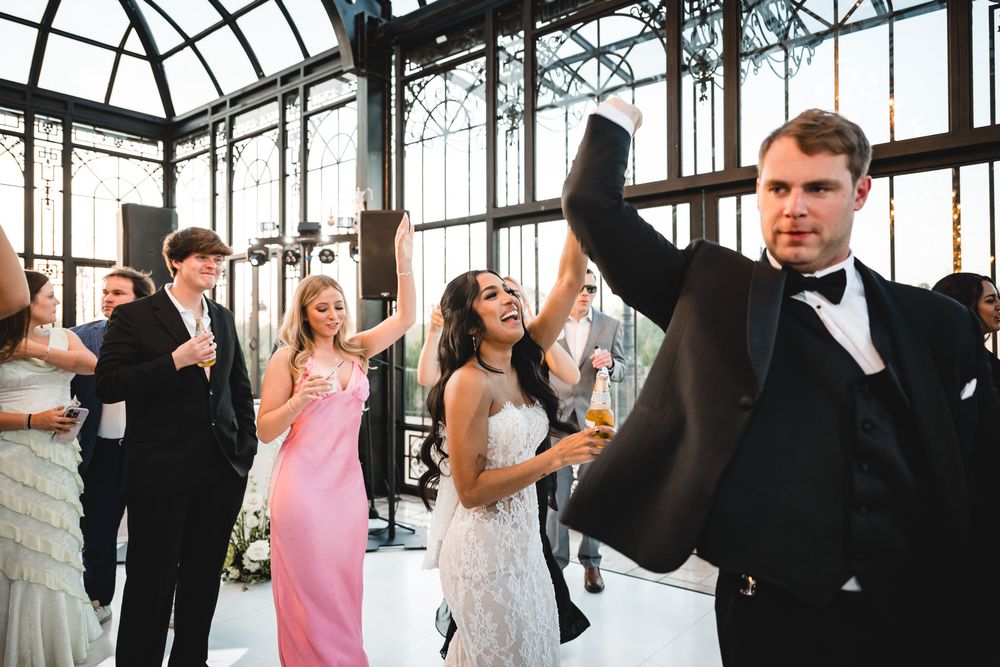 Wedding guests celebrate and dance in stunning glass conservatory venue during festive reception.