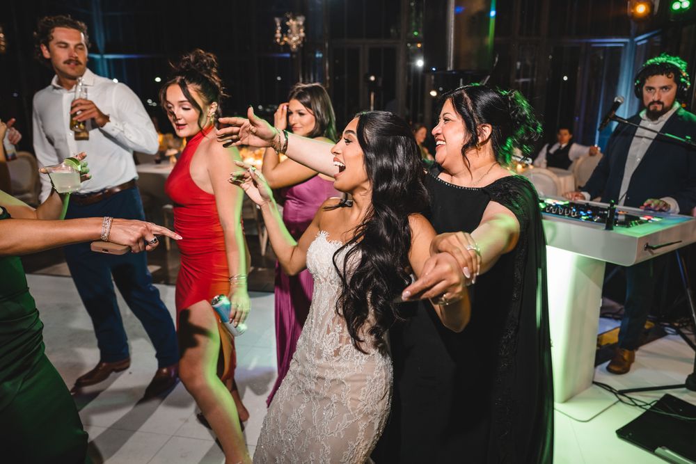 Bride celebrates with guests on dance floor near DJ booth during vibrant wedding reception.