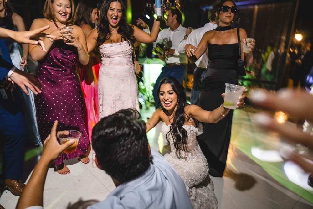 Bride in lace gown dances joyfully with guests at an outdoor wedding reception party.