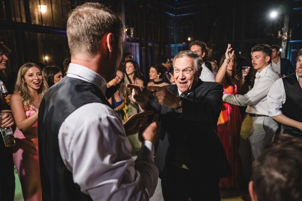 Energetic wedding reception dance floor with guests celebrating and dancing with the groom at a lively party.