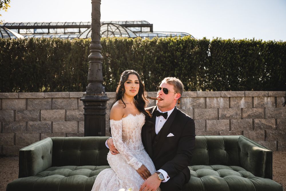 Bride and groom sitting together on a green velvet sofa outdoors at a wedding venue.