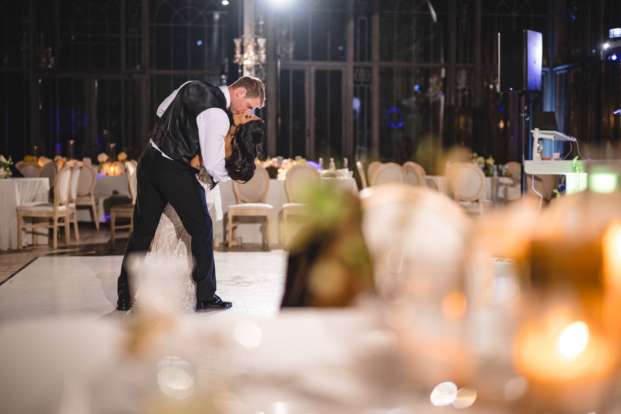 Groom performs energetic dance move on candlelit wedding reception dance floor.