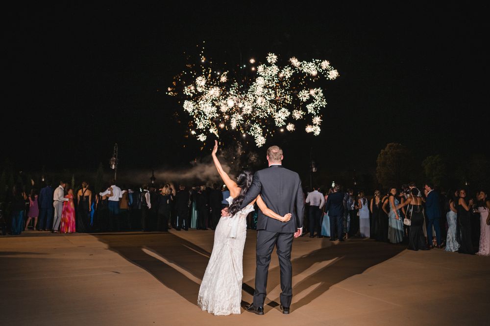 Newlyweds admire stunning floral firework display surrounded by guests at outdoor wedding celebration.
