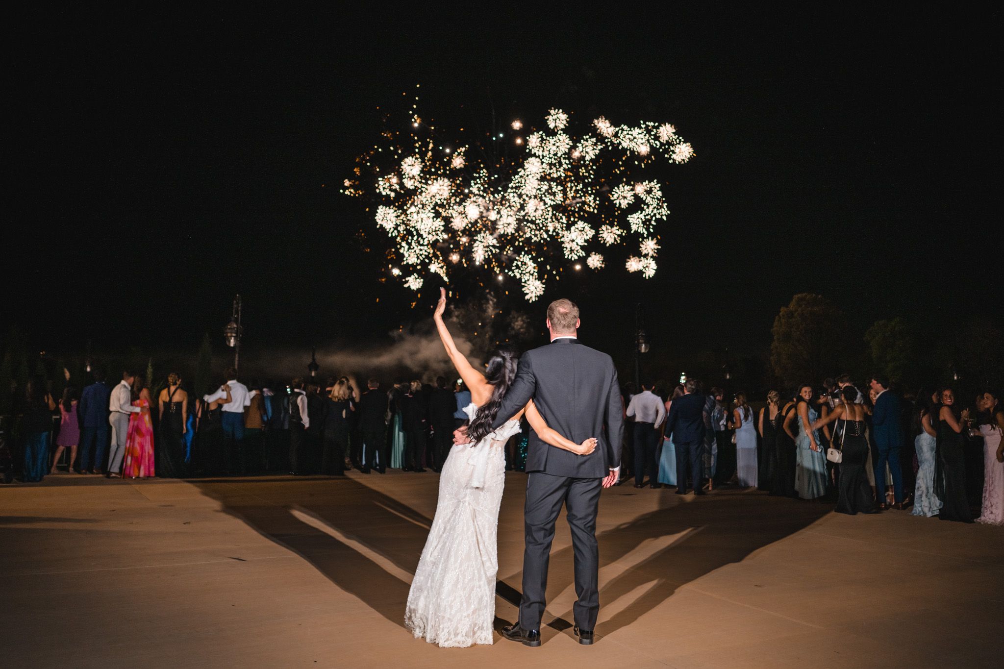 Newlyweds admire stunning floral firework display surrounded by guests at outdoor wedding celebration.