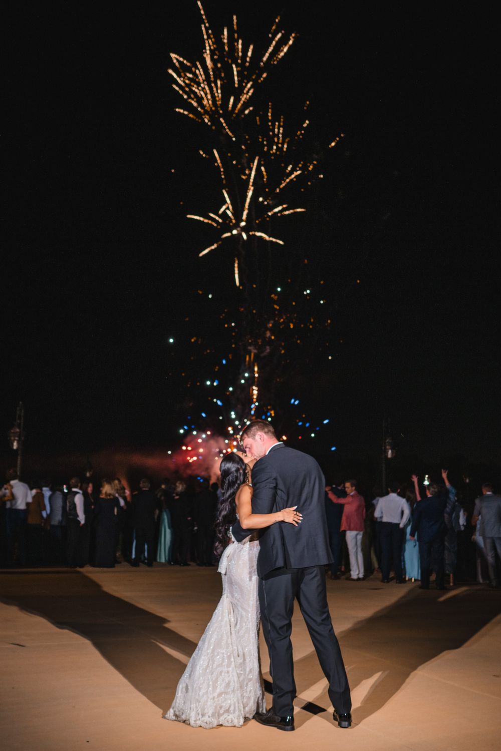 Bride and groom share romantic kiss under spectacular fireworks display at outdoor wedding.