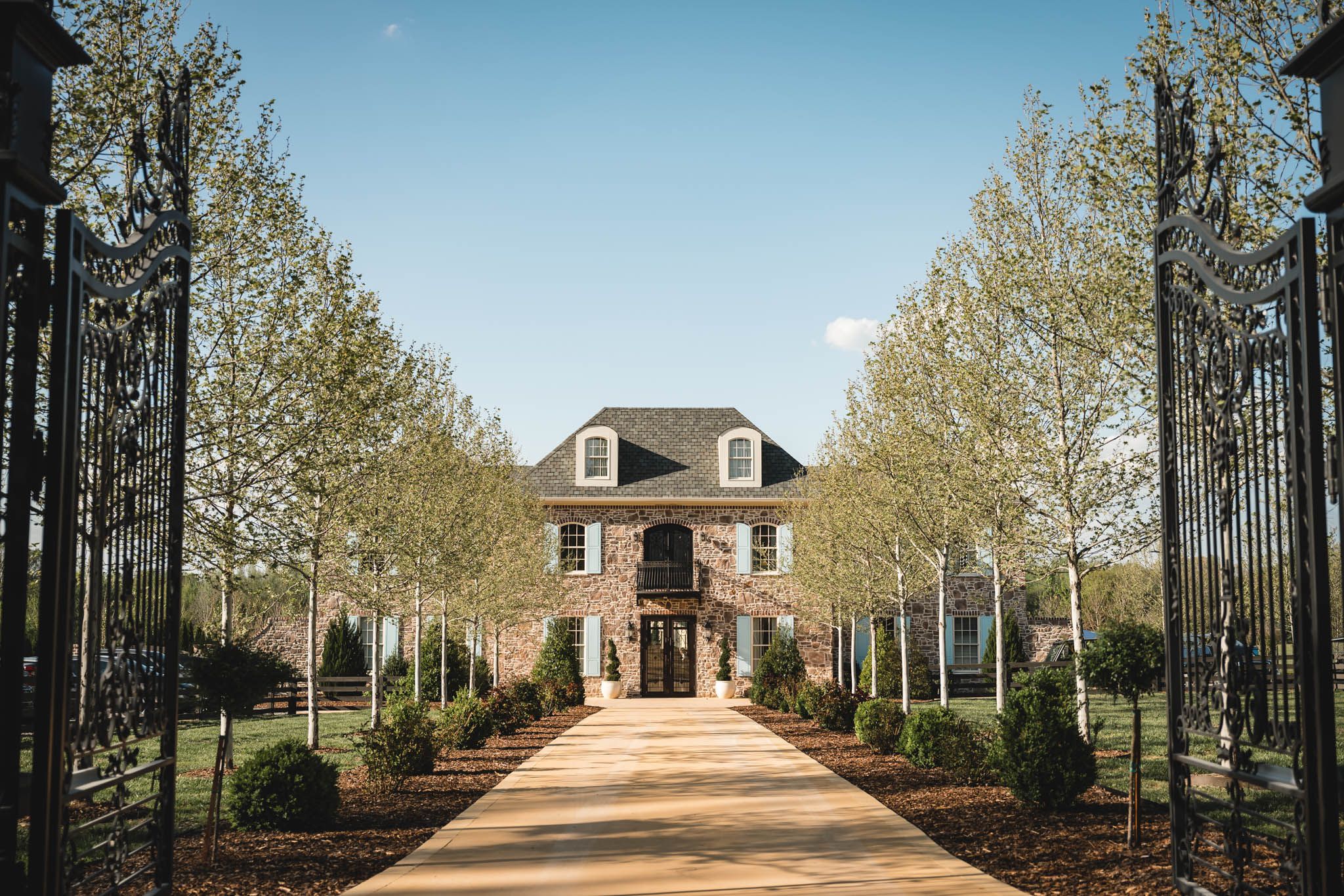 Elegant brick estate wedding venue framed by tall trees along a grand entrance driveway.