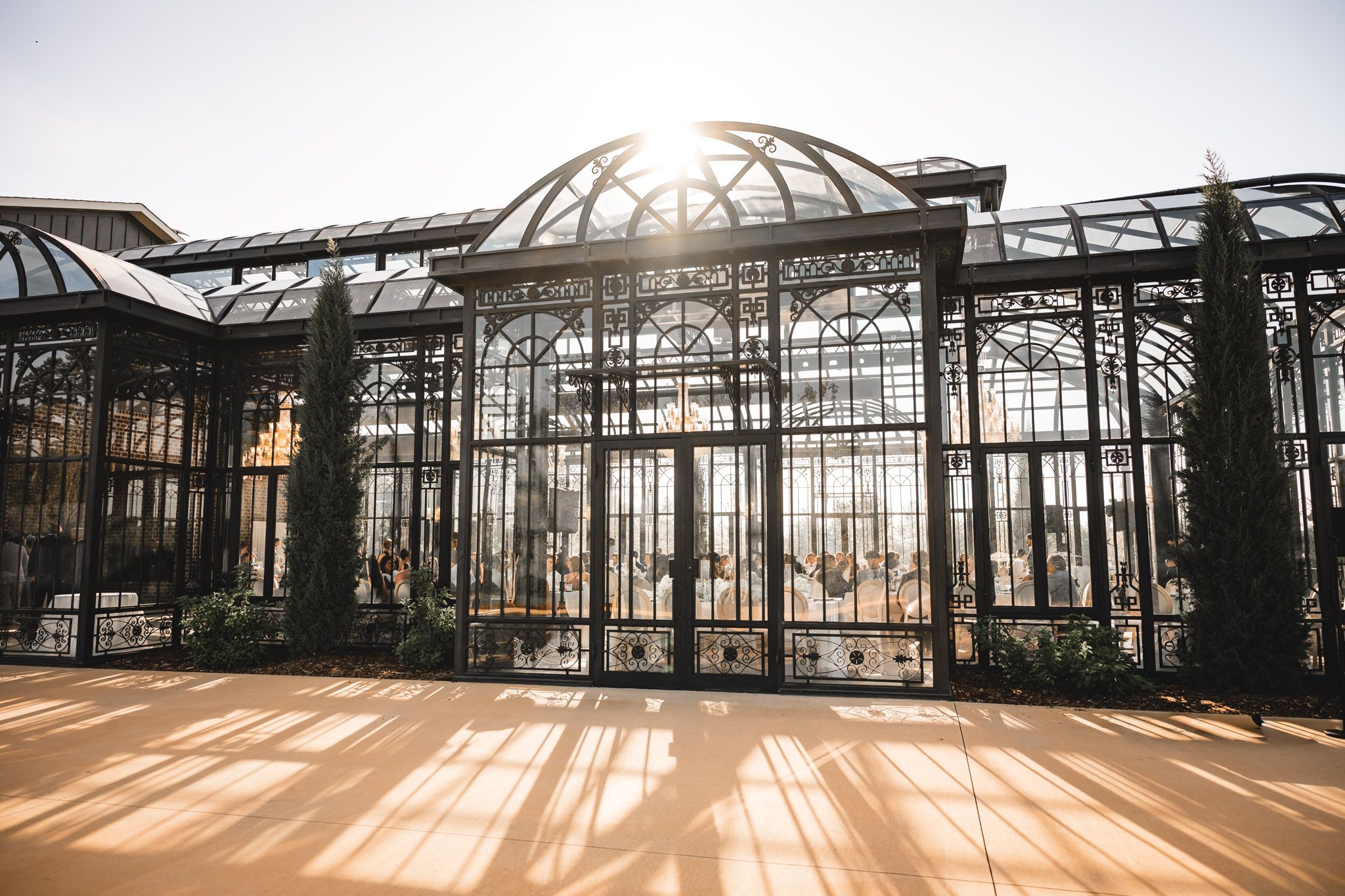 Stunning ornate glass greenhouse wedding venue glows in golden sunlight.