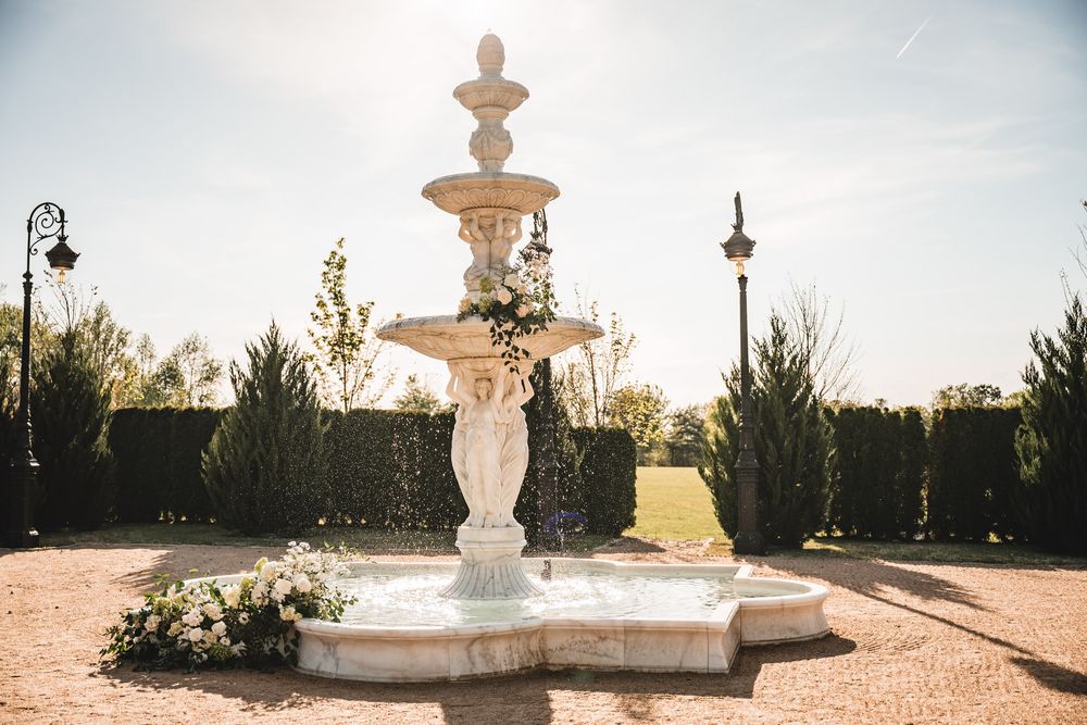 Elegant tiered stone fountain decorated with white flowers in manicured garden setting.