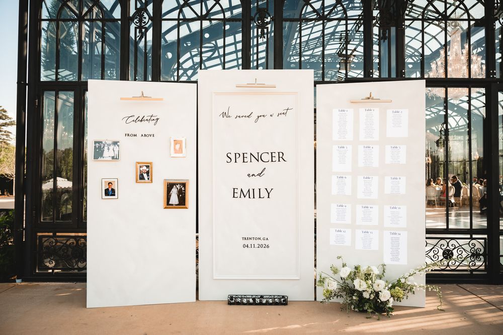 Elegant white tri-fold wedding seating chart display for Spencer and Emily with floral arrangements at a glass venue.
