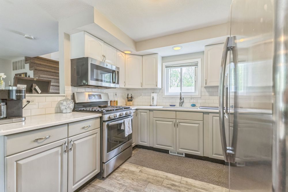 Modern kitchen with gray cabinets, stainless steel appliances, tile backsplash, and hardwood floors.