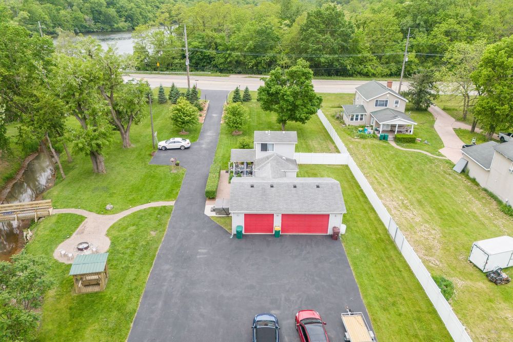 Aerial view of a residential property with a red garage, paved driveway, and lush green trees surrounding the home.