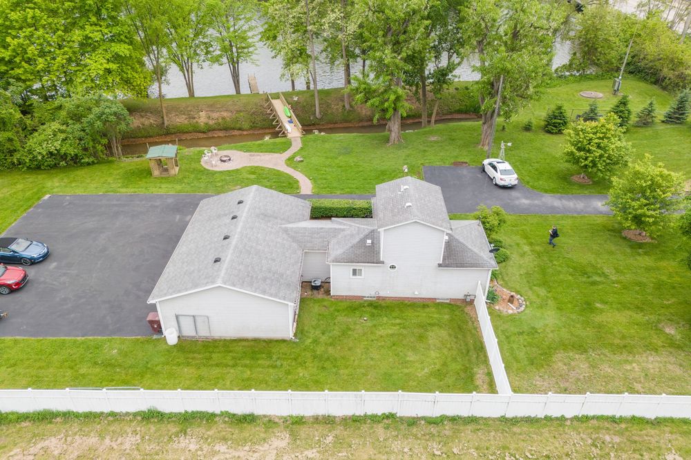 Aerial view of a suburban home with a large driveway, green lawn, and trees in the backyard.
