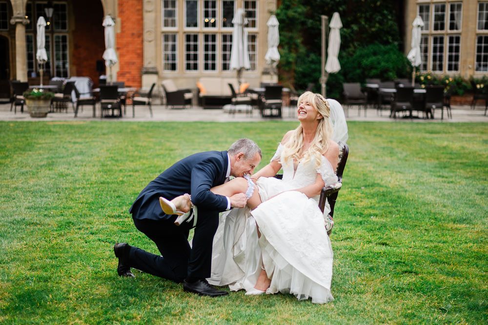 Groom kneeling to kiss bride's hand in a lush garden at an elegant wedding venue.
