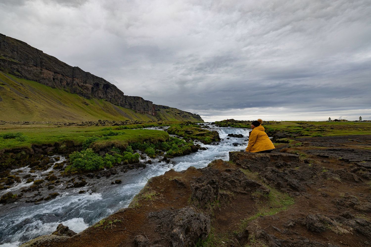 Sally Lombard sitting on a rock ledge at a small waterfall in Iceland