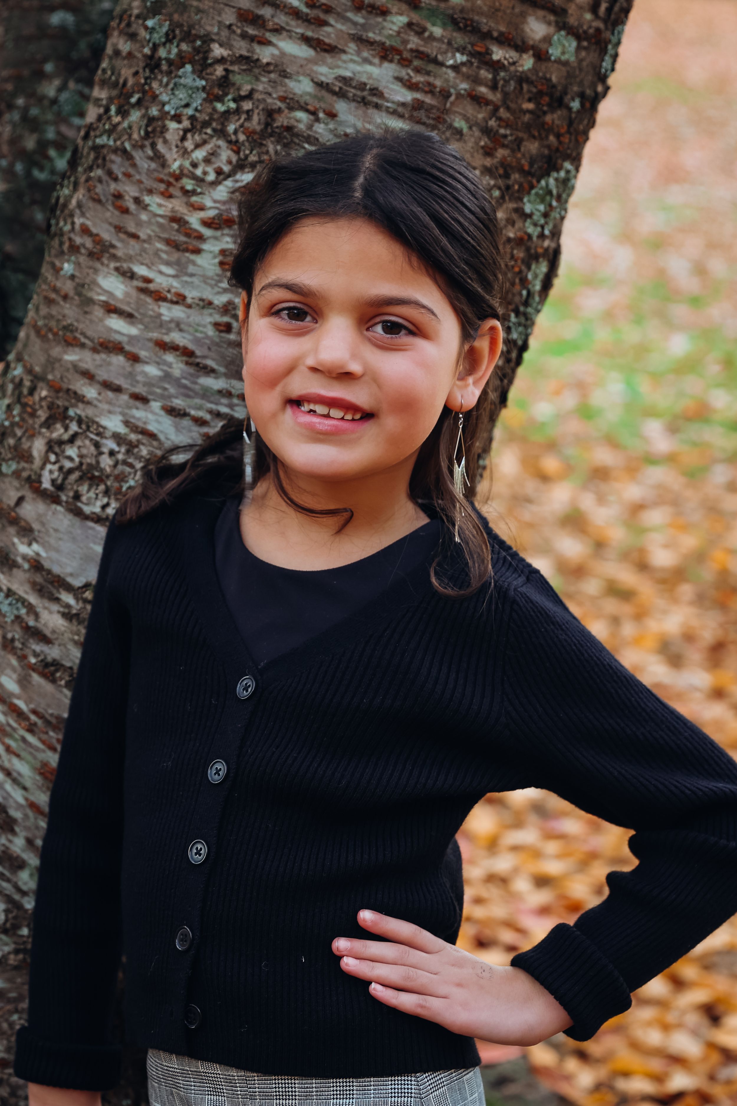 Person in black sweater poses playfully against autumn backdrop.