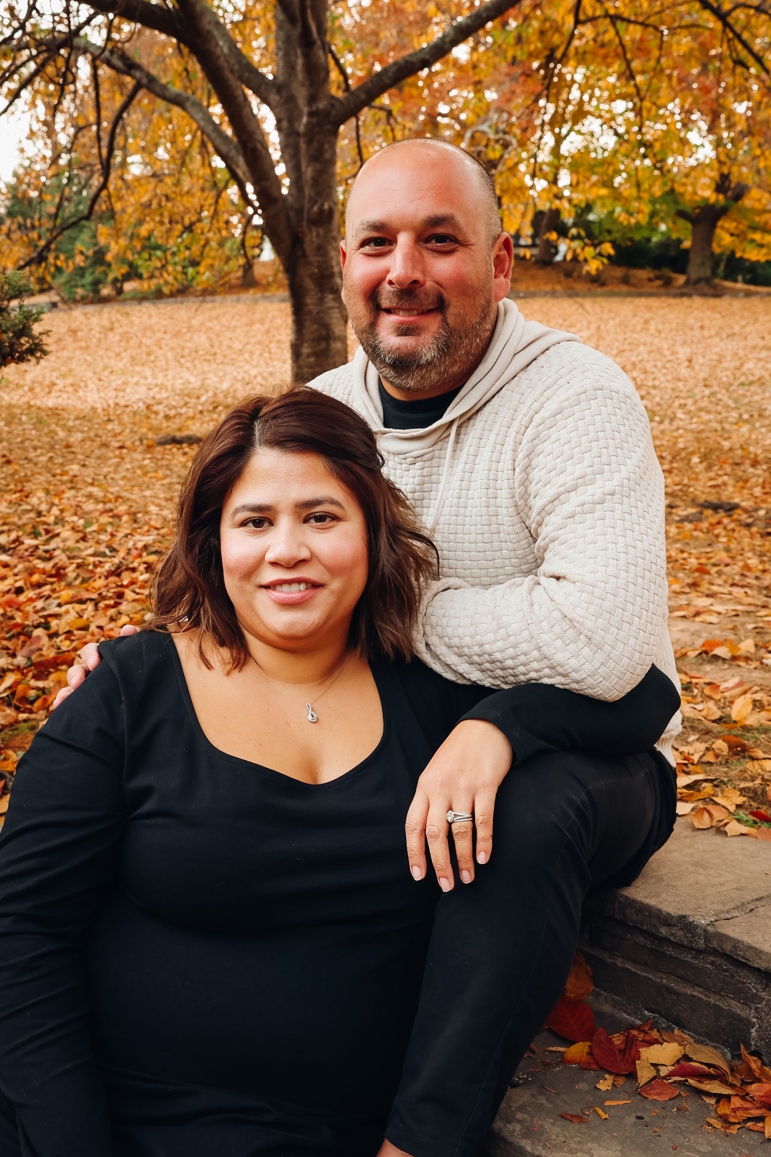Couple sits close together on stone steps during fall photo session with orange leaves around them.