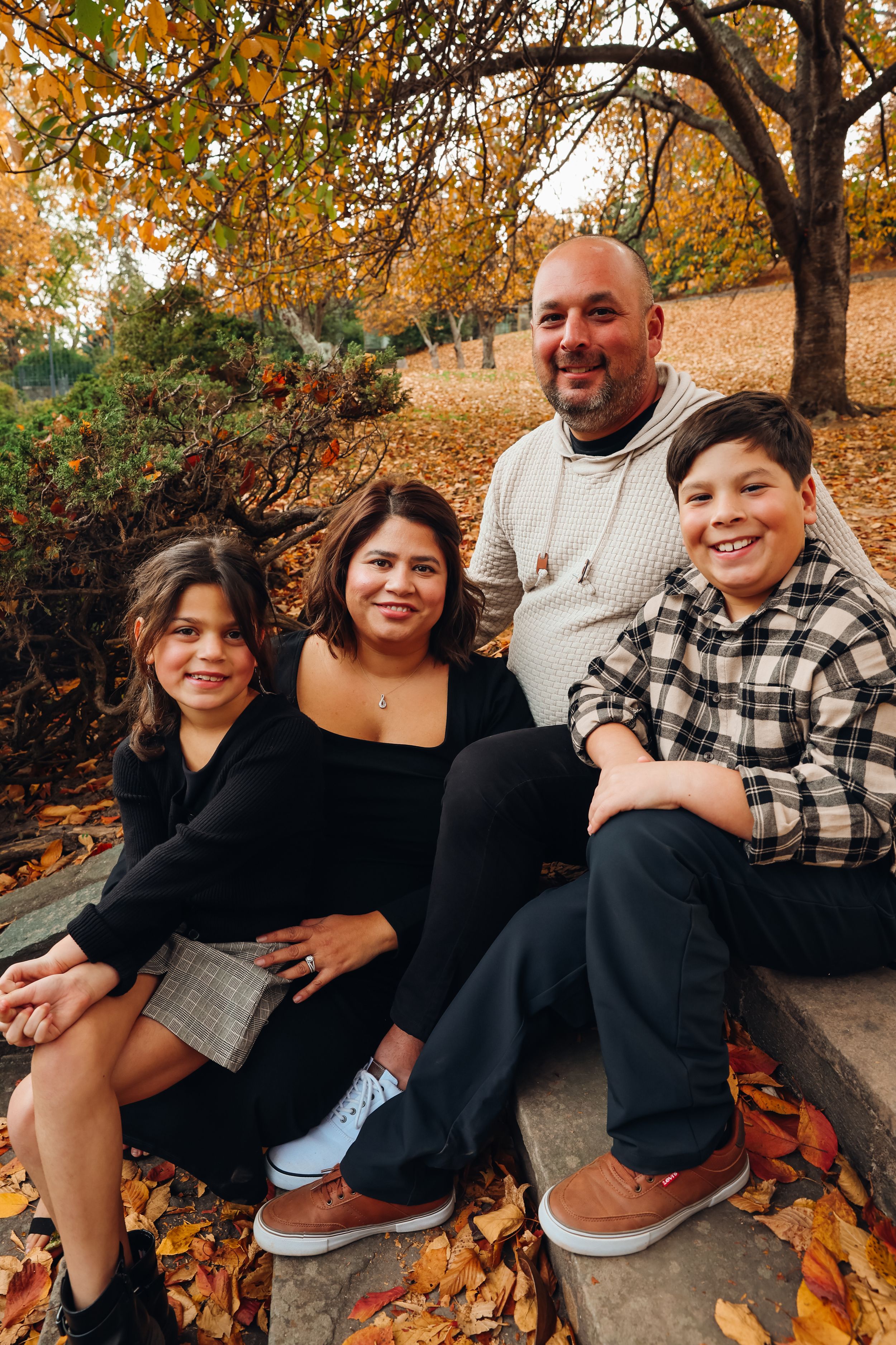 Family sitting together on stone steps surrounded by autumn leaves and trees.
