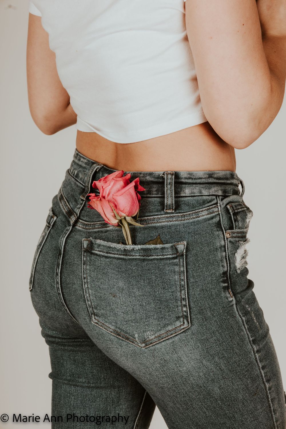 Close-up of woman in white crop top and jeans with a pink rose in back pocket.