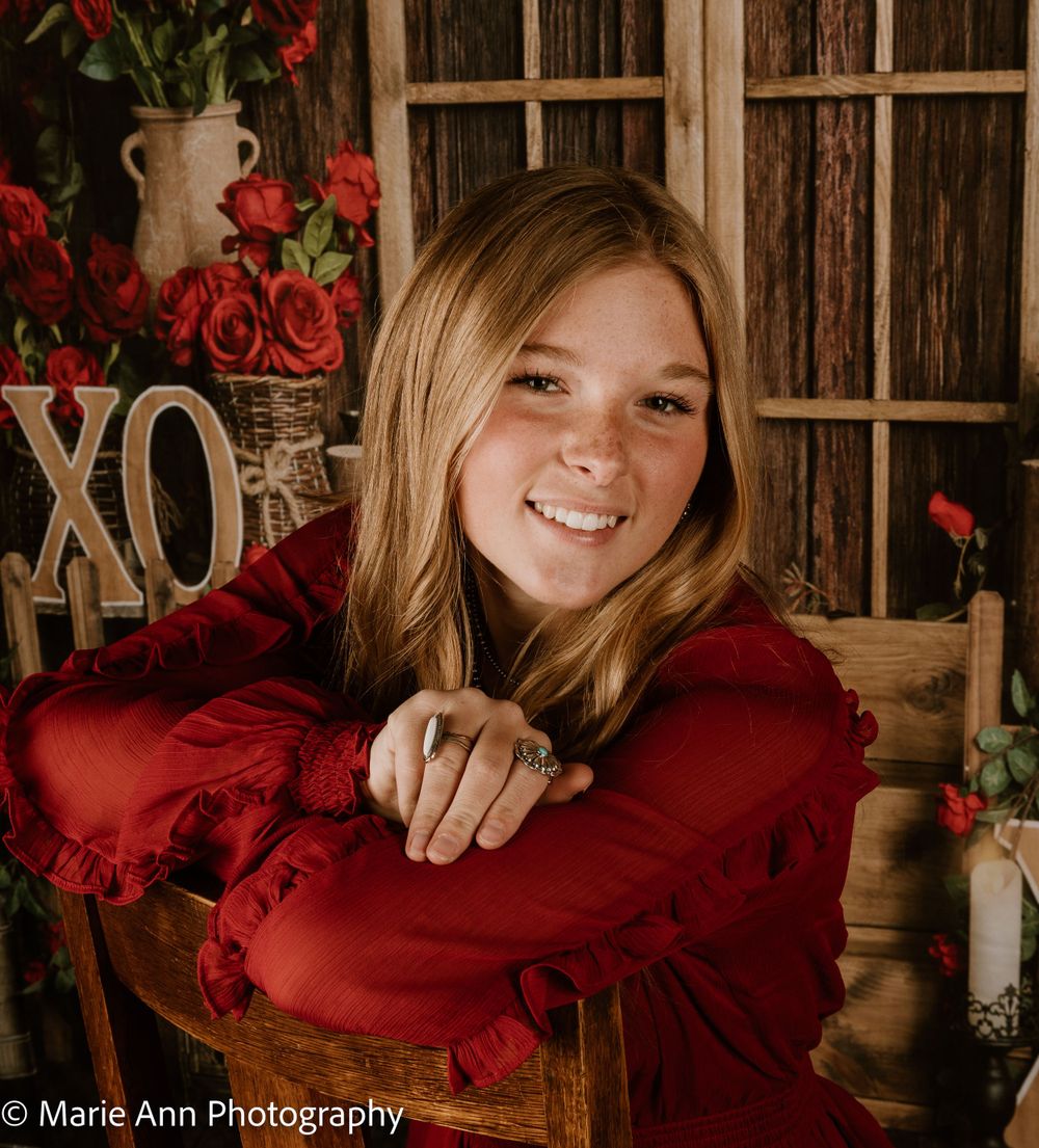 Smiling teenage girl in red dress posing with roses and XO sign for Valentine.