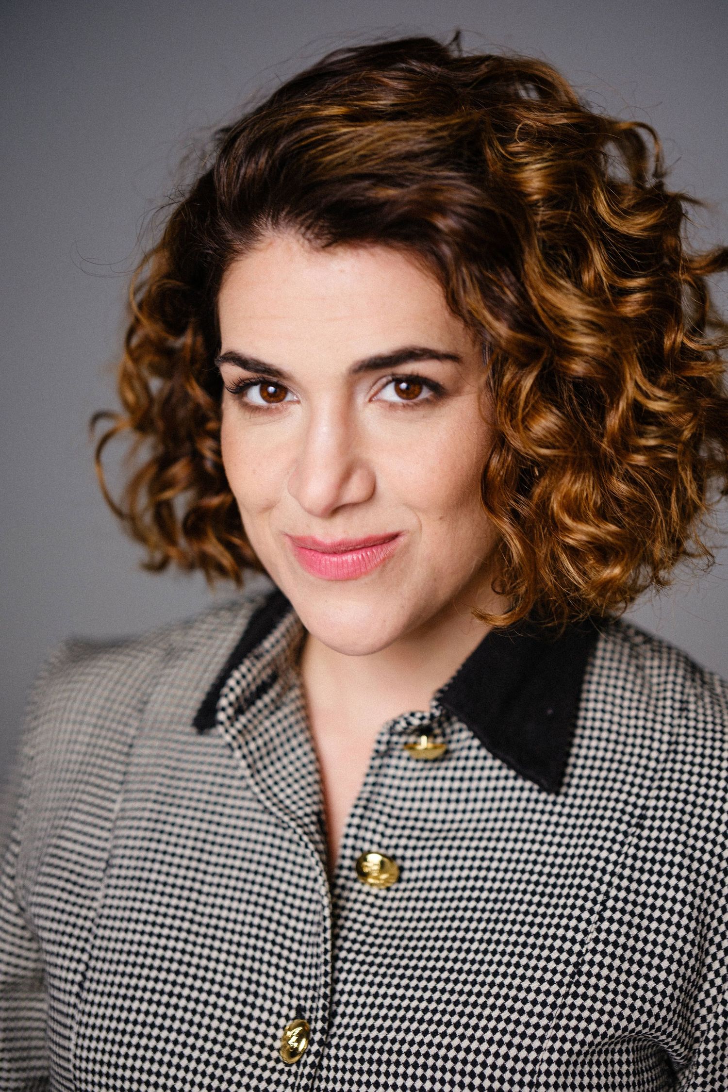 Headshot of a model wearing a houndstooth pattern top with gold buttons and curly hair.