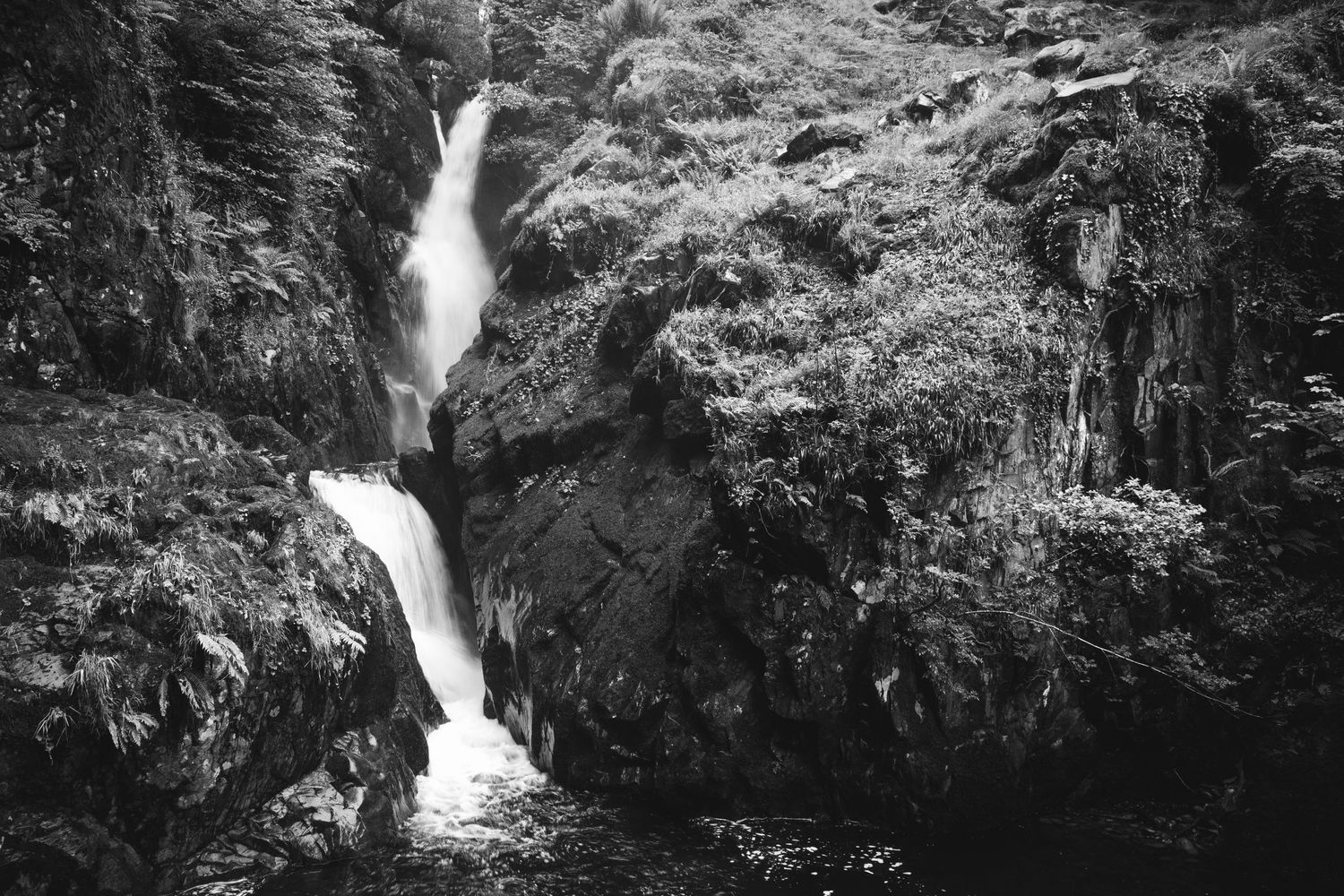 Dramatic black and white waterfall cascades down rocky cliffs surrounded by lush forest vegetation.
