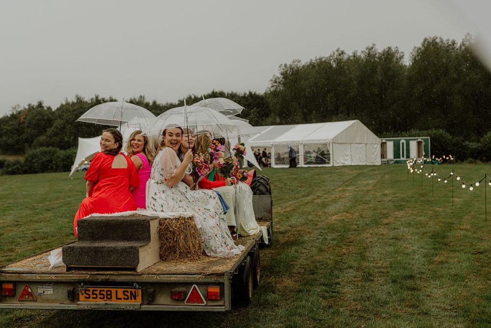 Wedding guests gathered under a white marquee tent with hay bales and rustic decor.