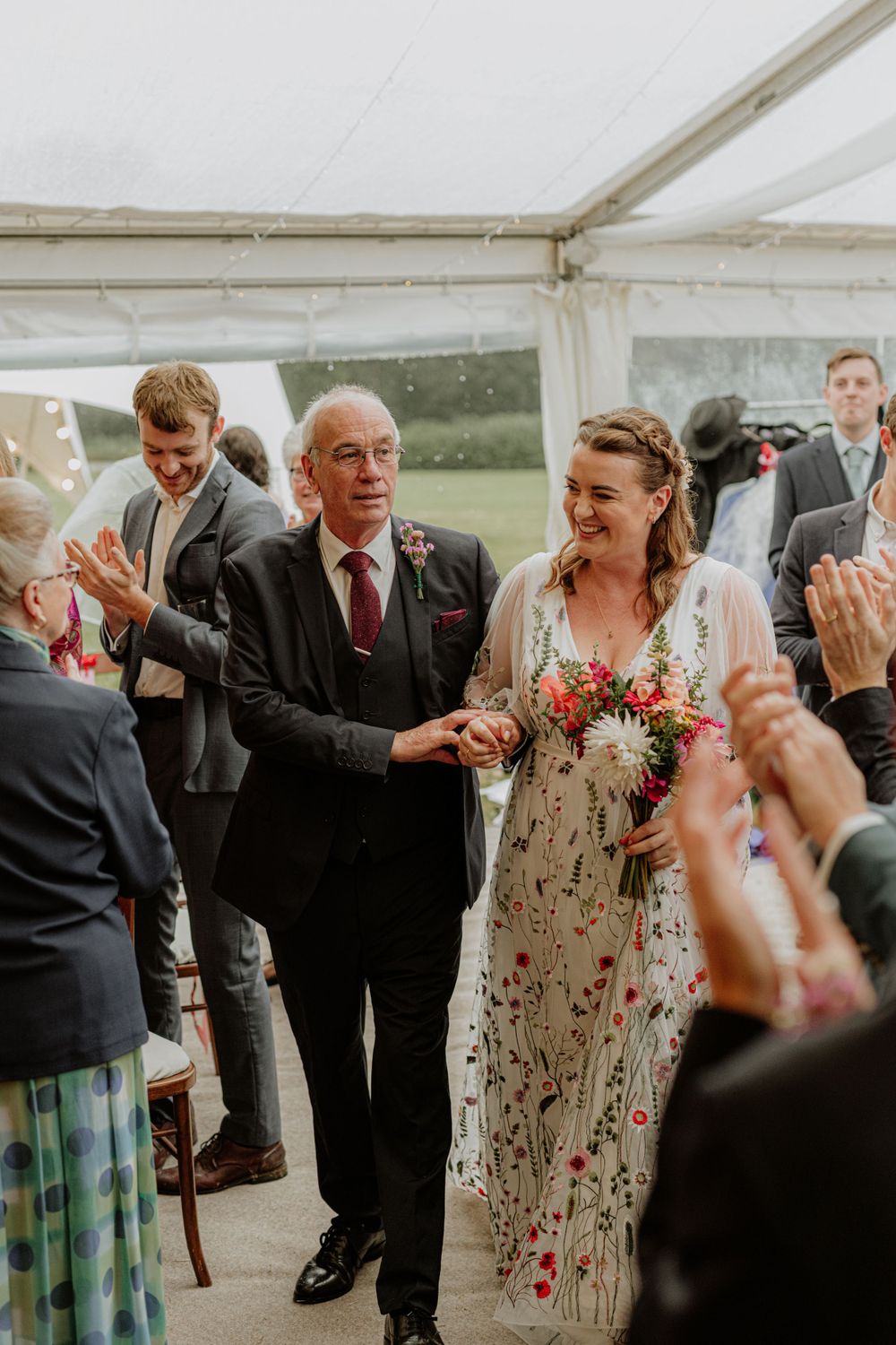 Wedding reception in a marquee tent with guests celebrating and floral decorations.