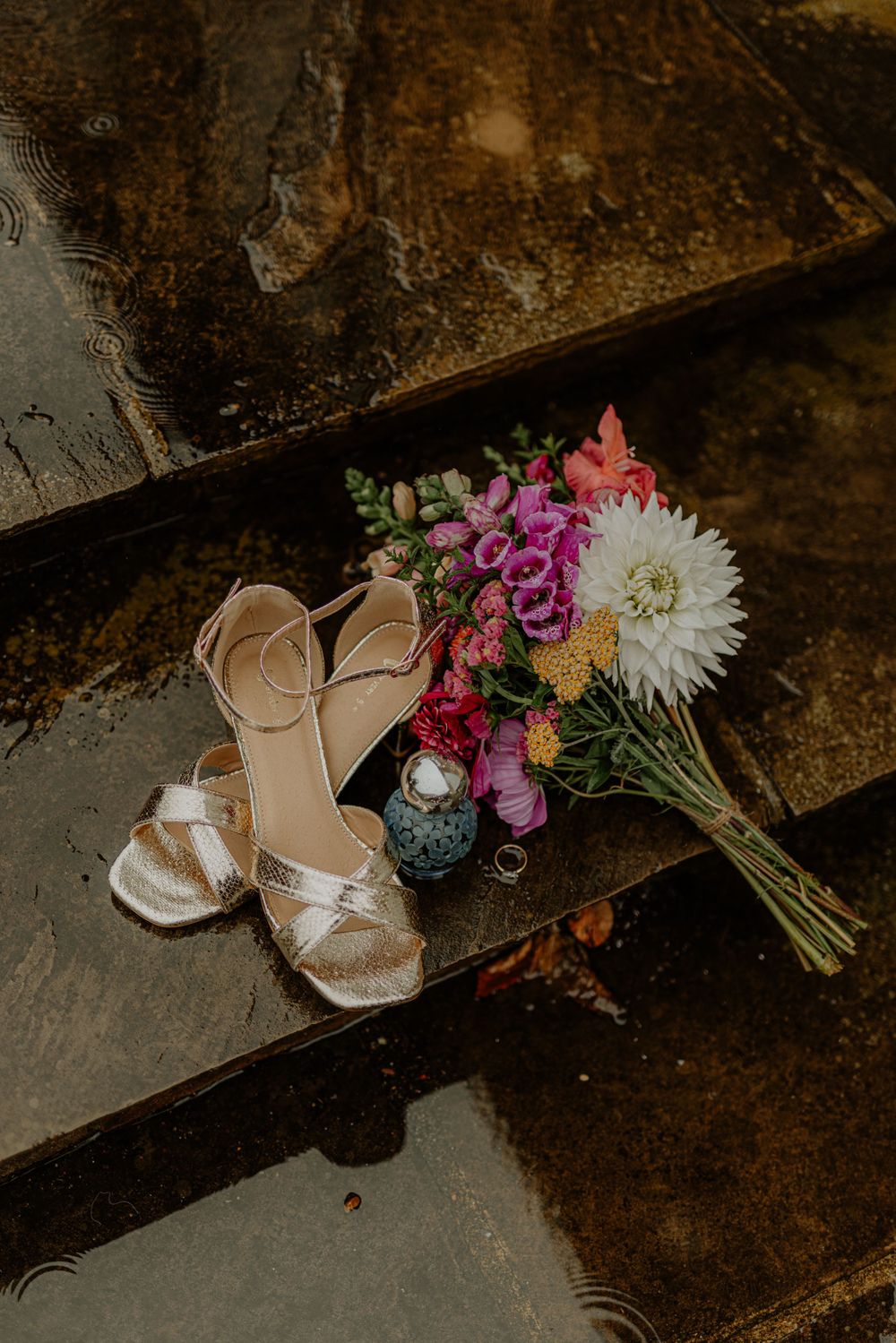 Wedding accessories including bridal shoes and colorful floral bouquet arranged on rustic steps.