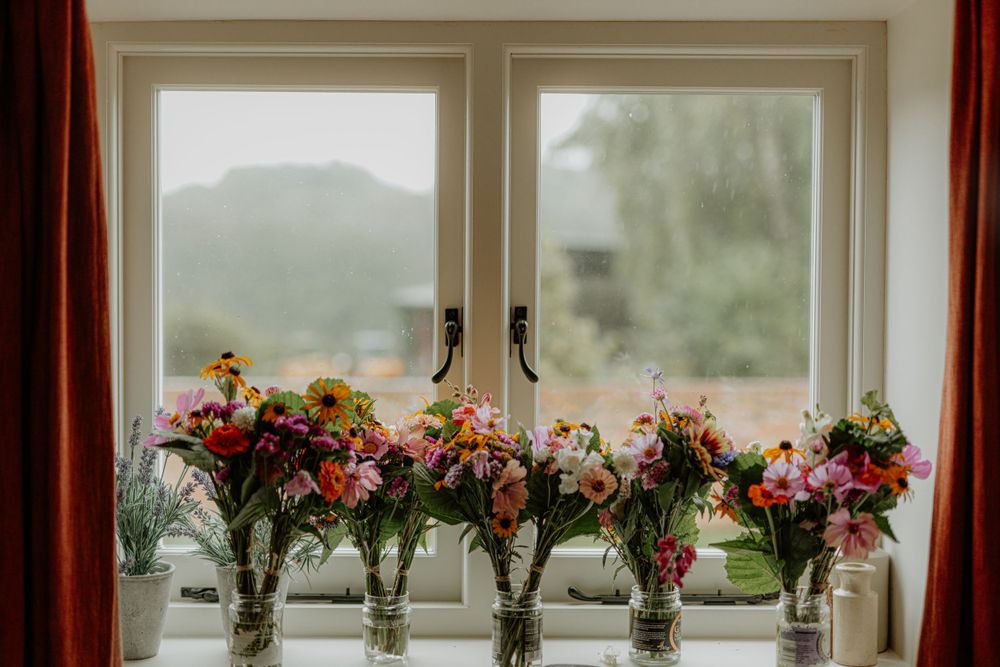 Window sill decorated with multiple colorful floral arrangements in glass vases.