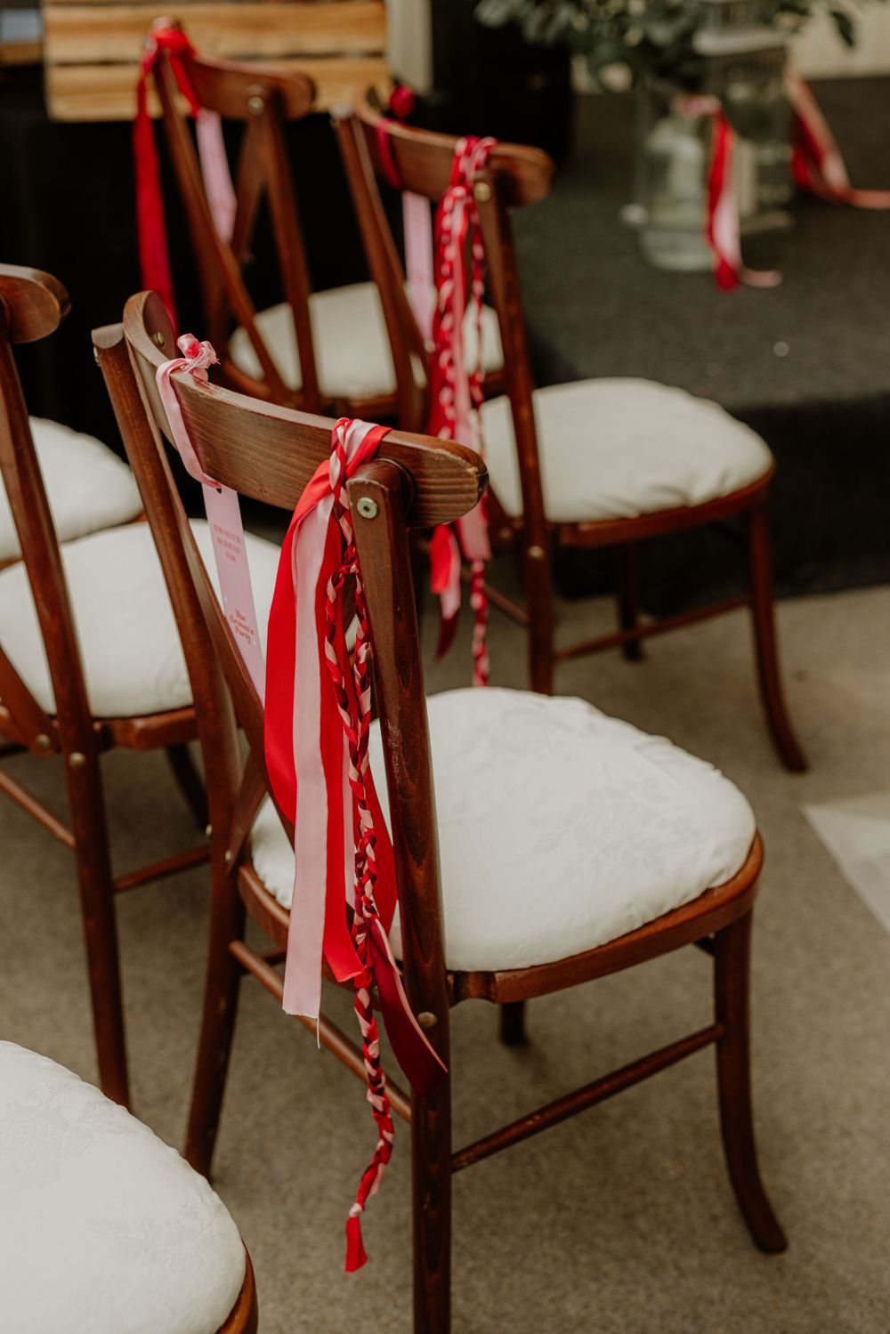 Elegant wooden chairs with white cushions decorated with red ribbons line up for a wedding ceremony.