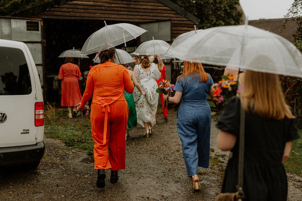 Wedding guests walking under umbrellas on a rainy day at an outdoor venue.