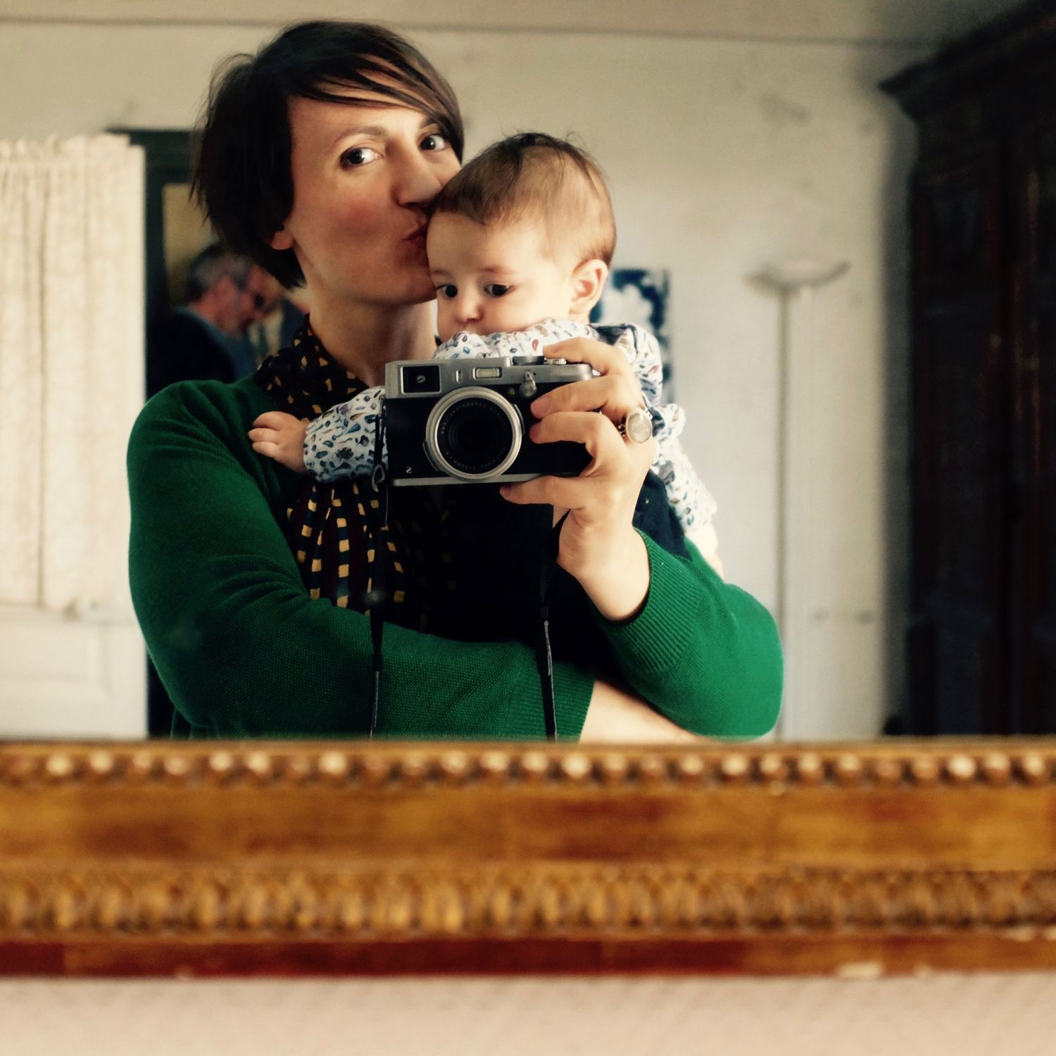 Une photographe tient un bébé dans ses bras et se prend en photo dans un miroir ancien avec un appareil photo Fujifilm